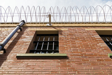 Prison walls with bars on windows surrounded by barbed wire