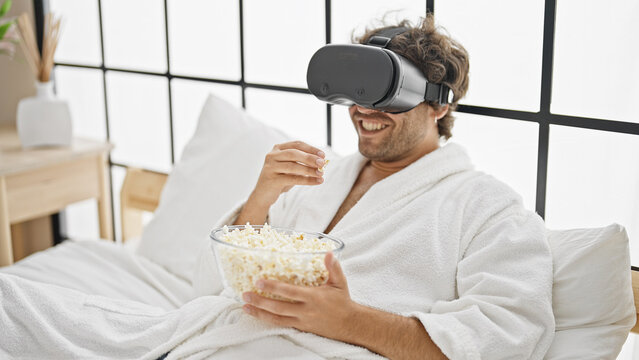 Young hispanic man watching movie using virtual reality glasses at bedroom
