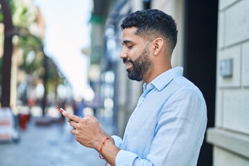 Young arab man smiling confident using smartphone at street