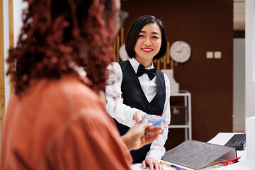 Woman paying for room reservation at hotel reception, using card and pos terminal for electronic...