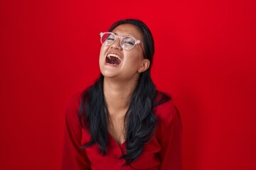 Asian young woman standing over red background angry and mad screaming frustrated and furious, shouting with anger. rage and aggressive concept.