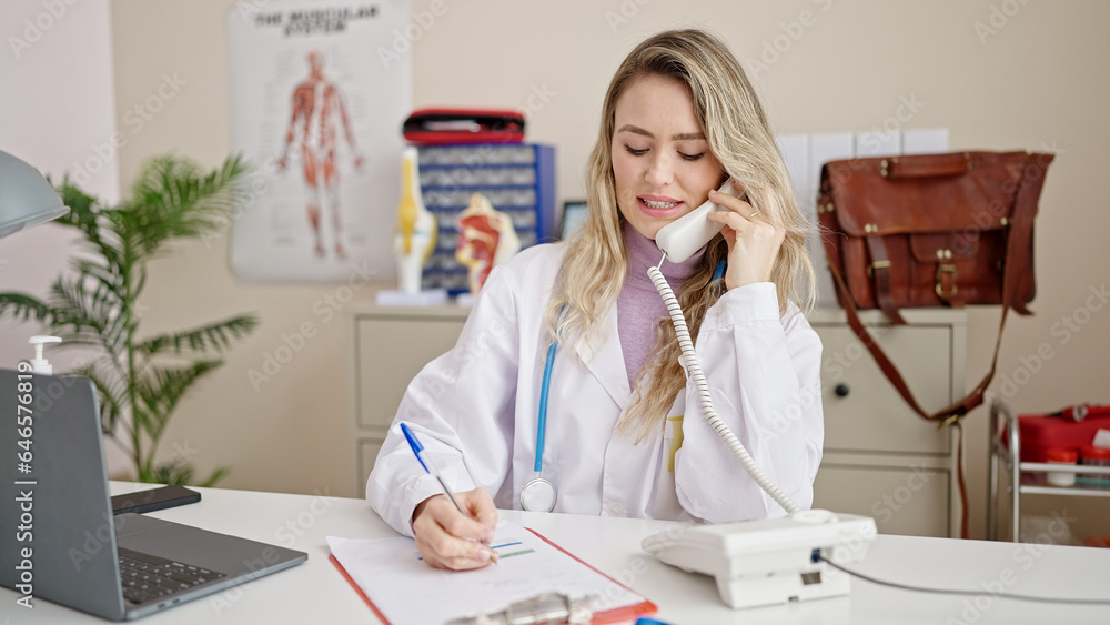 Poster young blonde woman doctor talking on telephone writing on document at clinic