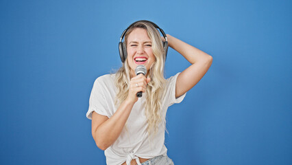 Young blonde woman listening to music singing song over isolated blue background