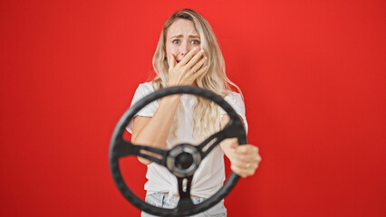 Young blonde woman using steering wheel as a driver stressed over isolated red background