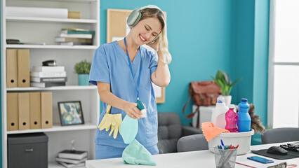 Young blonde woman professional cleaner cleaning table listening to music at the office