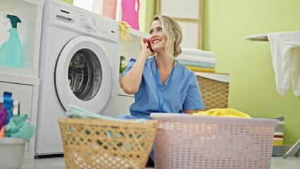 Young blonde woman professional cleaner talking on smartphone at laundry room