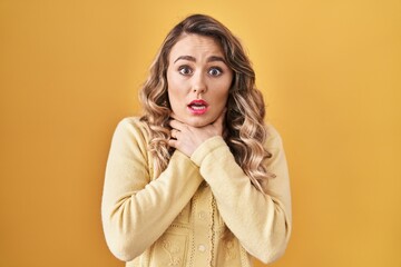 Young caucasian woman standing over yellow background shouting and suffocate because painful strangle. health problem. asphyxiate and suicide concept.