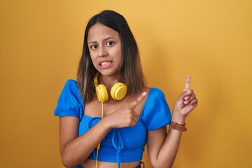 Hispanic young woman standing over yellow background pointing aside worried and nervous with both hands, concerned and surprised expression