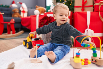 Adorable blond toddler playing with toys sitting on floor by christmas gifts at home