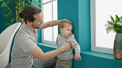 Father and son measuring child on wall at dinning room