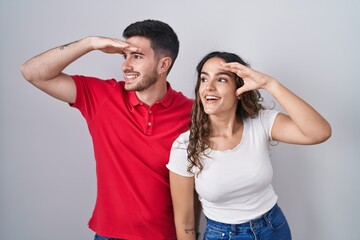 Young hispanic couple standing over isolated background very happy and smiling looking far away...
