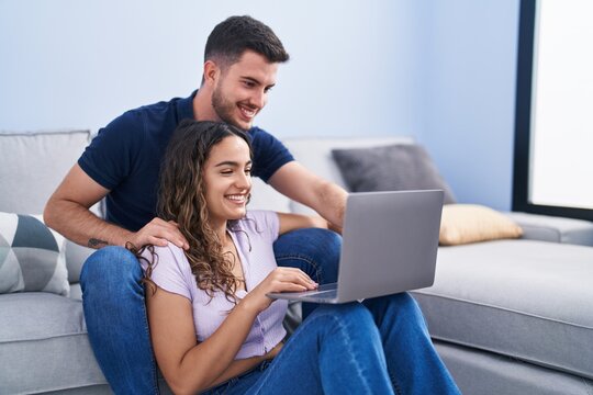 Young hispanic couple using laptop sitting on sofa at home