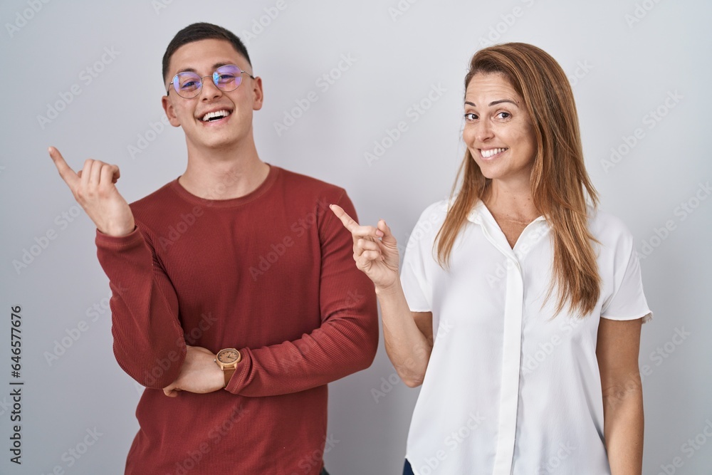 Wall mural mother and son standing together over isolated background with a big smile on face, pointing with ha