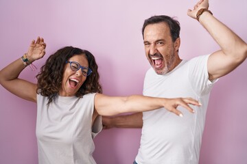 Middle age hispanic couple together over pink background dancing happy and cheerful, smiling moving...