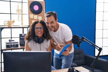 Man and woman musicians composing song using computer and touchpad at music studio