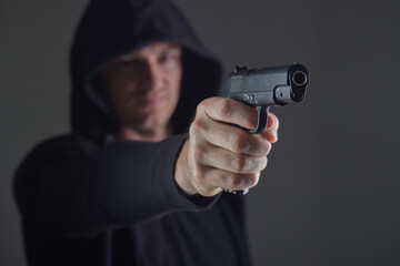 robber with gun aiming into camera. Man in hood threatens with firearm. Weapon in person's hands....