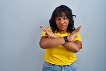 Hispanic woman standing over blue background rejection expression crossing arms doing negative...