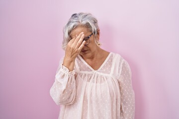 Middle age woman with grey hair standing over pink background tired rubbing nose and eyes feeling fatigue and headache. stress and frustration concept. - obrazy, fototapety, plakaty