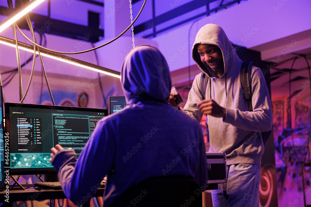 Poster hacker holding ssd drive with dangerous malware and explaining hacking attack plan to crime partner.