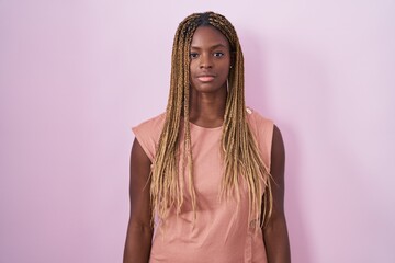 African american woman with braided hair standing over pink background relaxed with serious expression on face. simple and natural looking at the camera.