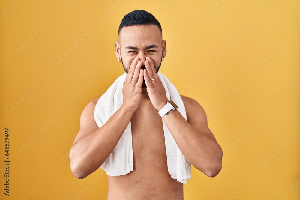 Poster young hispanic man standing shirtless with towel laughing and embarrassed giggle covering mouth with