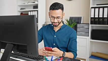 Young hispanic man business worker using computer and smartphone at the office