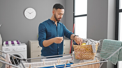 Young hispanic man hanging clothes on clothesline at laundry room