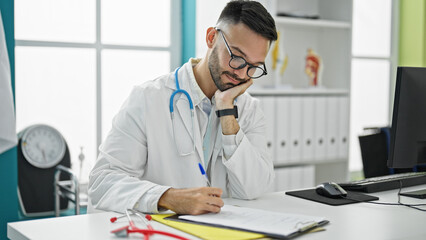 Obraz premium Young hispanic man doctor writing medical report on clipboard at the clinic