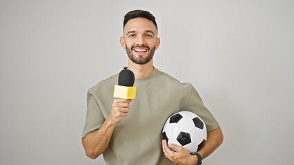 Young hispanic man soccer reporter working using microphone holding football ball over isolated white background