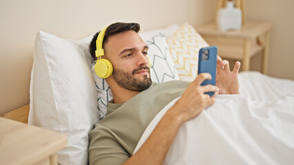Obraz premium Young hispanic man listening to music lying on bed at bedroom