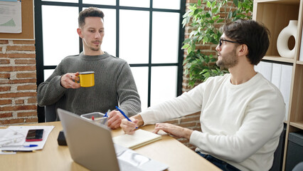 Two men business partners writing on notebook drinking coffee at office