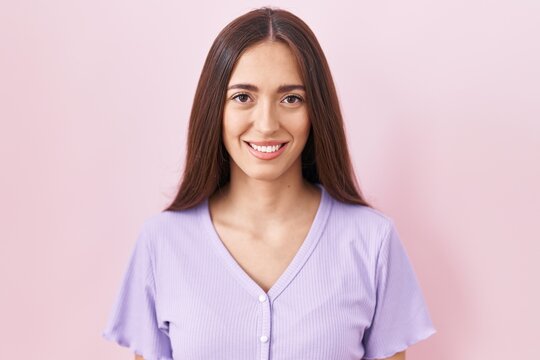 Young hispanic woman with long hair standing over pink background with a happy and cool smile on face. lucky person.
