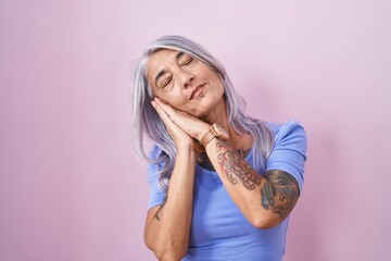 Middle age woman with tattoos standing over pink background sleeping tired dreaming and posing with...