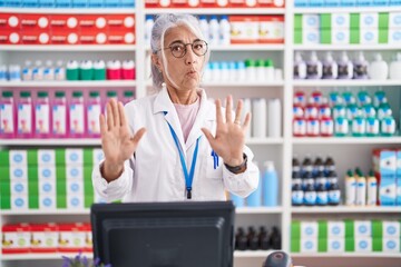 Middle age woman with tattoos working at pharmacy drugstore moving away hands palms showing refusal...
