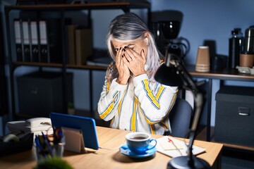 Middle age woman with grey hair working at the office at night with sad expression covering face with hands while crying. depression concept.