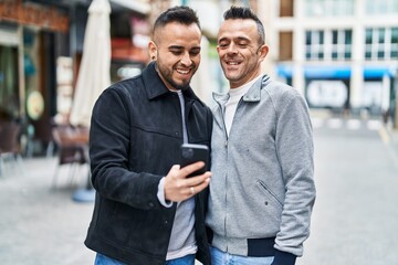 Two men couple smiling confident using smartphone at coffee shop terrace