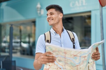 Young hispanic man student smiling confident holding city map at street
