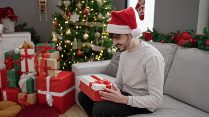 Young hispanic man smiling confident holding christmas gift at home