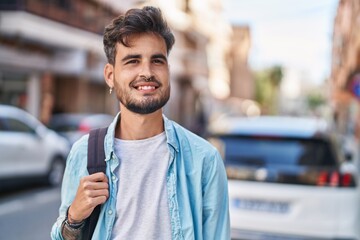 Young hispanic man student smiling confident wearing backpack at street