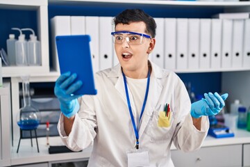 Non binary person working at scientist laboratory using tablet scared and amazed with open mouth...