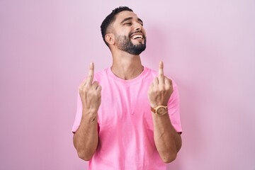 Hispanic young man standing over pink background showing middle finger doing fuck you bad...