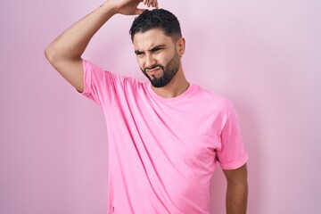 Hispanic young man standing over pink background confuse and wondering about question. uncertain...