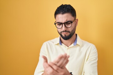 Hispanic young man wearing business clothes and glasses suffering pain on hands and fingers,...
