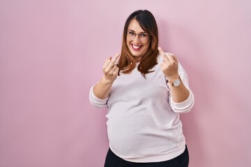 Pregnant woman standing over pink background showing middle finger doing fuck you bad expression,...