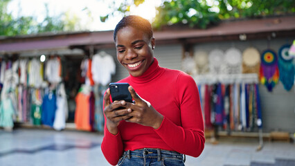 African american woman using smartphone smiling at street market