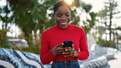 African american woman using smartphone smiling at park