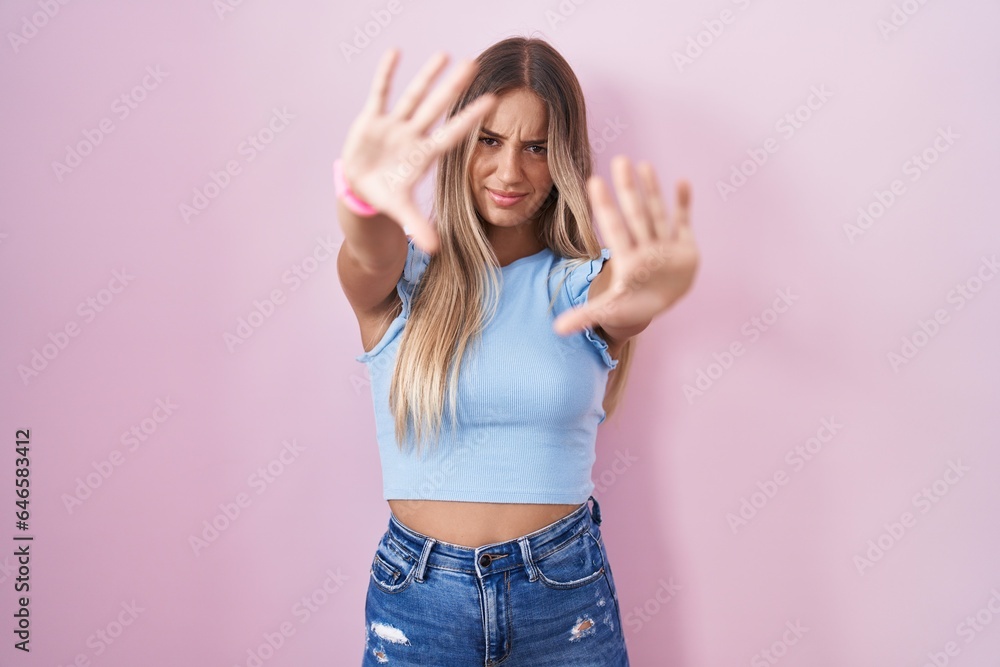 Poster young blonde woman standing over pink background doing frame using hands palms and fingers, camera p