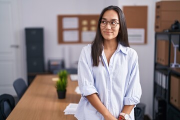 Young hispanic woman at the office smiling looking to the side and staring away thinking.