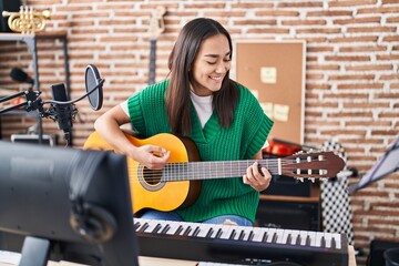 Fototapeta na wymiar Young hispanic woman musician playing classical guitar at music studio
