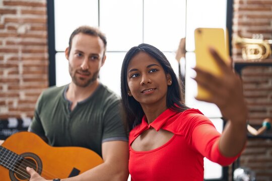 Man and woman musicians playing classical guitar make selfie by smartphone at music studio